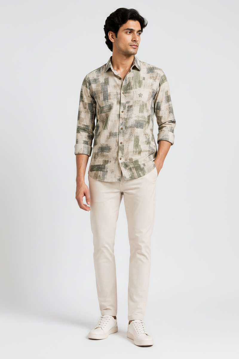 A man modeling a long-sleeve button-up shirt with an abstract camouflage-like print in beige, gray, and muted green, paired with light beige trousers and white sneakers. The image includes a full-body view, a closer torso view, and a close-up of the shirt collar and chest area.